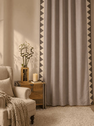 Beige armchair with a blanket, small table with a candle and plant, and a fantasy land curtain from lifencolors with geometric pattern in a room.