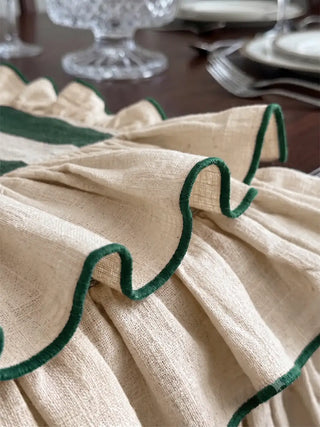 Close-up of the Florentine ruffle table runner in dark green, showing the corded green edging and the texture of the gathered ivory linen on a dining table.