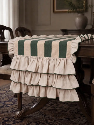 Detail of the Florentine ruffle table runner in dark green, showing the three tiers of green-edged linen ruffles falling over the end of a carved dining table.