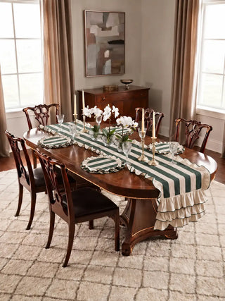 Florentine ruffle table runner in dark green on a polished oval dining table with matching ruffled placemats, crystal glassware, brass candlesticks and white orchids.