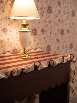 The Florentine Ruffle table runner in peach and rust stripes with a cream ruffled edge and rust piping, draped over a dark wood table.