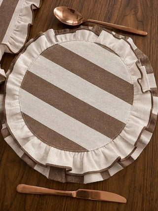 Close-up top view of Florentine Ruffles round table mat in beige and mocha diagonal herringbone stripe with a gathered ruffle edge, on a dark walnut table beside rose gold cutlery