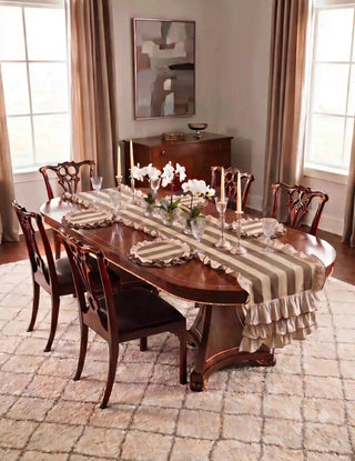 Florentine Ruffles table mats in beige and mocha set on a mahogany Chippendale dining table with a coordinating striped ruffled runner, crystal glassware, ivory taper candles, and white orchids