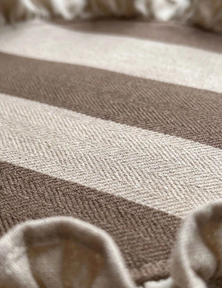 Macro close-up of Florentine Ruffles table mat surface showing the fine herringbone weave texture of the diagonal mocha and ivory stripes and the softly gathered mocha-bound ruffle edge