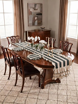 Florentine ruffles table mats in dark green set on a polished oval dining table with a matching ruffle runner, crystal glassware, brass candlesticks and white orchids.