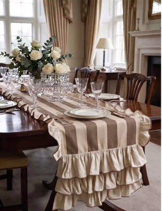 Florentine Ruffles table runner in beige and mocha laid along a mahogany dining table in a classical English dining room with crystal glassware, white rose centrepiece, cream curtains, and Chippendale chairs