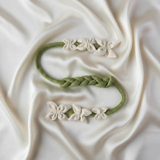 Flat lay of the Floret Braid Tassel, showing the thick green cord and the two clusters of small white fabric flower knots on a silk background.