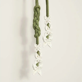 Close-up of the Floret Braid Holdback hanging, highlighting the chunky braided section of the olive green rope and the white fabric florets.
