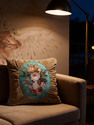 The Florid Verona Bloom cushion styled on a tan sofa in a moody room under warm lamplight.