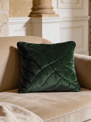A luxury forest green quilted velvet cushion styled on a beige velvet sofa next to a classical column.