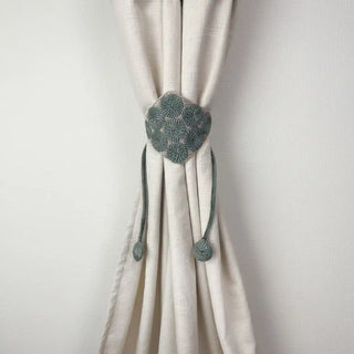 Forest Orbit Handcrafted Curtain Tieback secured around a cream curtain, showing the diamond-shaped panel with green spiral embroidery.