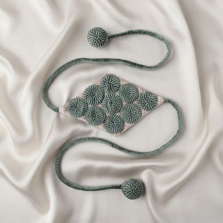 Flat lay of the Forest Orbit Tassel, showing the diamond panel with repeating spirals and the thick cords with woven ball ends.