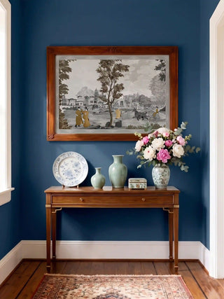 The French Life art print styled in a dark wood frame on a navy blue wall above a console with celadon vases.
