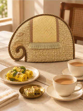 The Gajraja tea cosy on a linen-covered tea table with cups of chai, an elephant in gold brocade with a fringed chevron saddle.