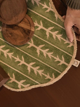 The Garden Gala placemat in green with cream leaf sprigs, fine cream stripes and a textured tan border, styled on a dark wood table.