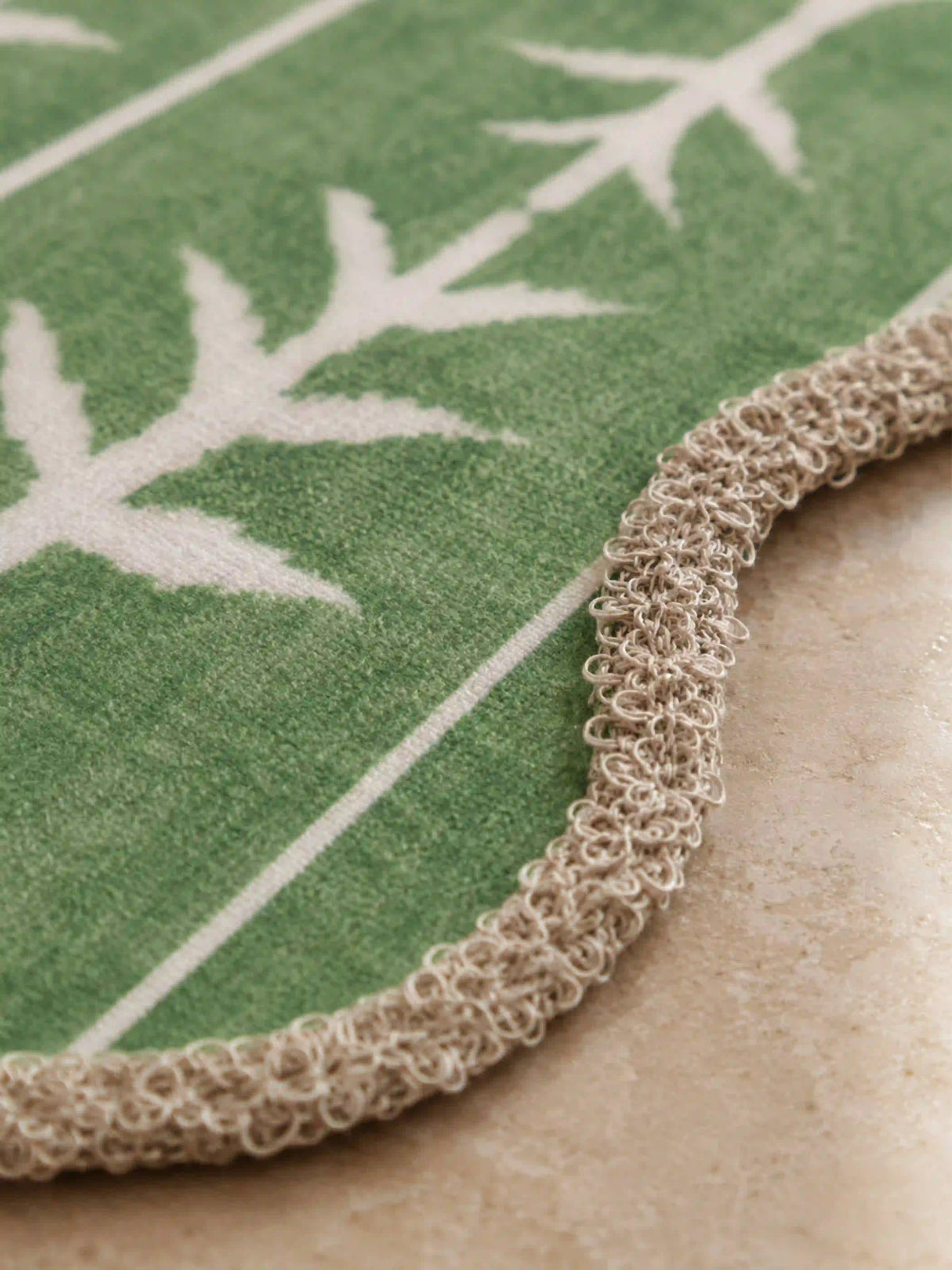Close-up of a looping corded scallop trim and green botanical branch embroidery on table linen