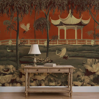 An orange oriental garden wallpaper featuring a pagoda pavilion, flying cranes, lotus flowers, and trees, styled behind a wooden console with a lamp.