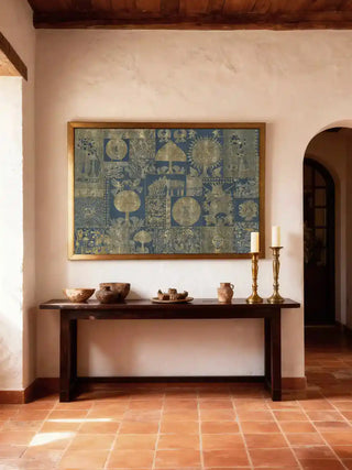 Geet Madhubani wall art in indigo and gold, framed in antique gold above a dark wood console with earthen bowls and brass candlesticks in a terracotta-tiled foyer.