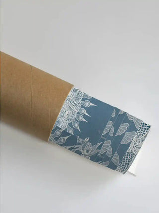 Geet Madhubani wall art print in indigo and white rolled in a kraft shipping tube, showing the fine white sun and peacock linework.