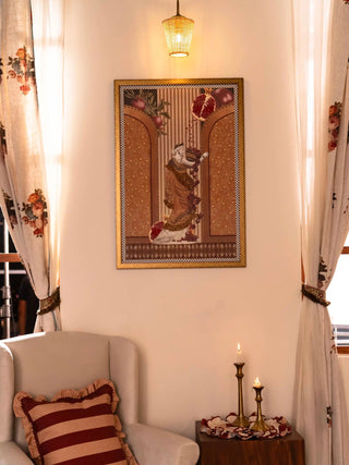 The Gilded Mythos wall art in a gold frame, showing a draped classical figure and pomegranates between two arches, on a cream wall.