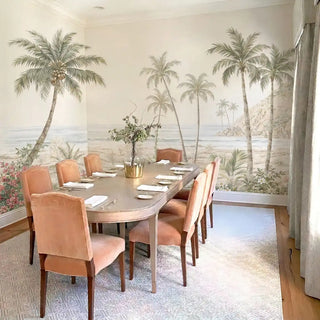 The Goa Coastal Romance tropical wallpaper mural wrapping two corner walls inside a luxury dining room with peach velvet chairs.