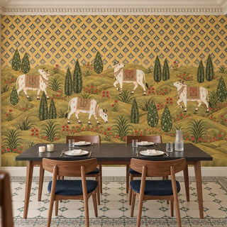 The Gokul Reverie Pichwai wallpaper behind a black-topped dining table with walnut chairs and navy seats, cows and cypress trees above view-dining