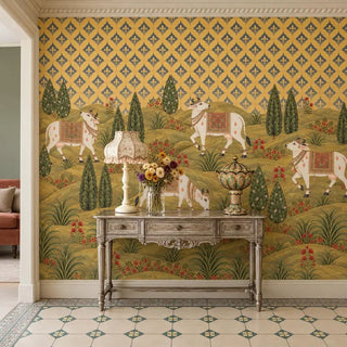 The Gokul Reverie wallpaper in an entryway behind a carved grey console with a fringed lamp and a vase of flowers, cows grazing beyond view-foyer
