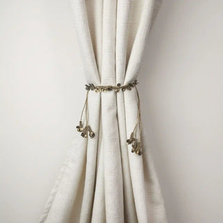 Regal Gilt Handcrafted Curtain Tieback cinched around a cream curtain, demonstrating the delicate, ornamental style of the metallic chain.