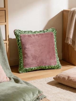 A luxury plum-toned velvet cushion with a gold scalloped embroidered border styled on a white armchair against a botanical mural.