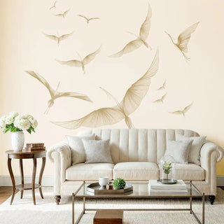 A cream wallpaper featuring golden abstract bird-like wing forms in flight, styled behind a neutral-toned sofa with modern decor.