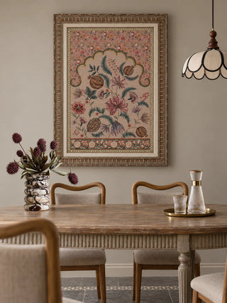 The Golestan Garden botanical wall art in a carved frame above a wooden dining table, with woven-back chairs and a brass drinks tray.