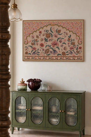 The Golestan wall art landscape in Blush Pink framed above a sage green glass-front cabinet, styled with a burgundy vase and glassware.