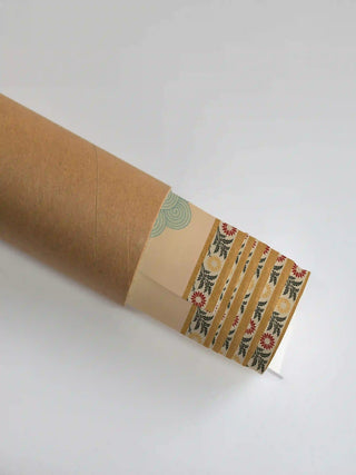 The Gopuram wall art print partly unrolled from its shipping tube, showing a spiral scroll field beside a striped floral border in peach, blue and mustard.