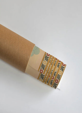 The Gopuram wall art print partially unrolled from its kraft paper shipping tube, showing a spiral scroll field beside a striped floral-and-frond border in peach, blue and mustard.