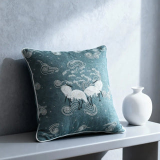 Single Graceful Cranes Azure Cushion Cover displayed on a grey bench with a white vase.