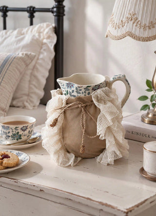 The Grandeur Ruffle jug cover in Taupe, view-bedside on a floral jug beside a teacup and lamp.