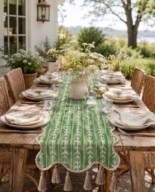 The Green Gala block-printed sage green table runner with thick jute tassels styled on a dark wood dining table inside a bright dining room.