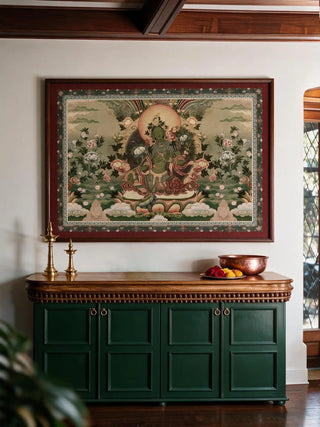 The Green Tara wall art in a dark wood and maroon-matted frame, hung above a carved wooden sideboard with brass lamps and a copper bowl.