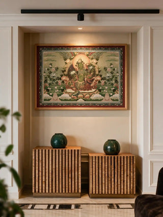 The Green Tara wall art in a wood frame, displayed in a niche above a wooden console with two dark green ceramic vases.