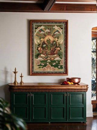 The Green Tara wall art in a dark wood and maroon-matted frame, hung above a green sideboard with brass lamps and a copper bowl.