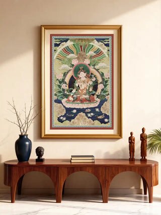 The Green Tara wall art in a gold frame, displayed above a wooden arched console with carved wooden figures and a dark vase.