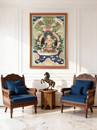The Green Tara wall art in a gold frame, hung above two carved wooden armchairs with navy cushions and a bronze horse figurine.