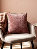 A Gulabi Bagh cushion cover in dusty rose velvet with architectural quilted patterns resting on a contemporary grey armchair.