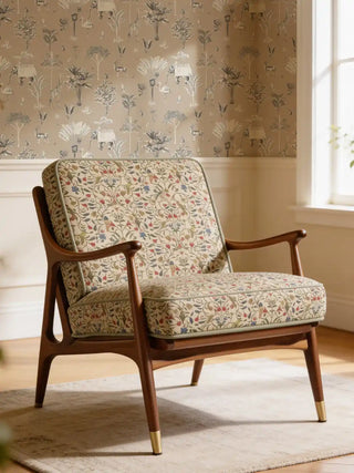 A luxury mid-century modern armchair upholstered in Gulbahar Beige fabric featuring hand-painted birds and vines against a safari wallpaper.