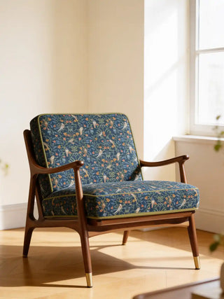 A luxury mid-century modern armchair upholstered in Gulbahar Blue fabric featuring hand-painted birds and botanical vines.