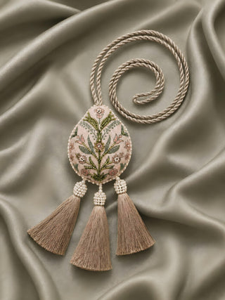 A flat lay view of the Gulbano curtain tie back against warm champagne satin fabric, showcasing the full length of the braided loop cord.