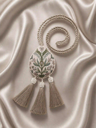 A flat lay view of the Gulbano curtain tie back against warm champagne satin fabric, showcasing the full length of the braided loop cord.