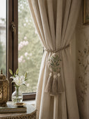 The Gulbano hand-embroidered teardrop tie back gathering a cream linen curtain panel neatly next to a window frame.
