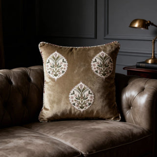Gulmohar Noor Buta Cushion styled on a brown leather tufted sofa in a dimly lit room.