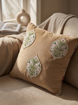 The Gulmohar Patra cushion styled on a neutral linen armchair in a sun-drenched, luxury interior.